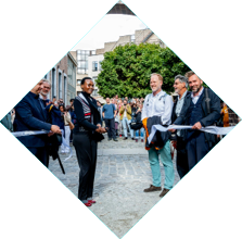Een groep mensen staat buiten op een straat met kasseien terwijl een persoon een lint doorknipt en anderen toekijken en fotograferen.

Beschrijving gegenereerd door AI